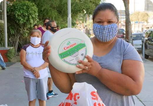 Woman in line for free groceries with a wheel of cheese